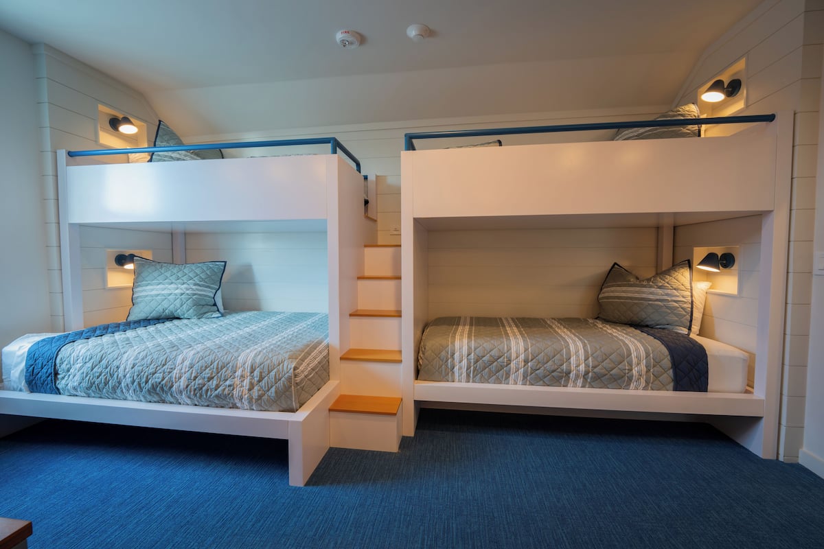 Two bunk beds with built-in desks and nightstands, each with a lamp.