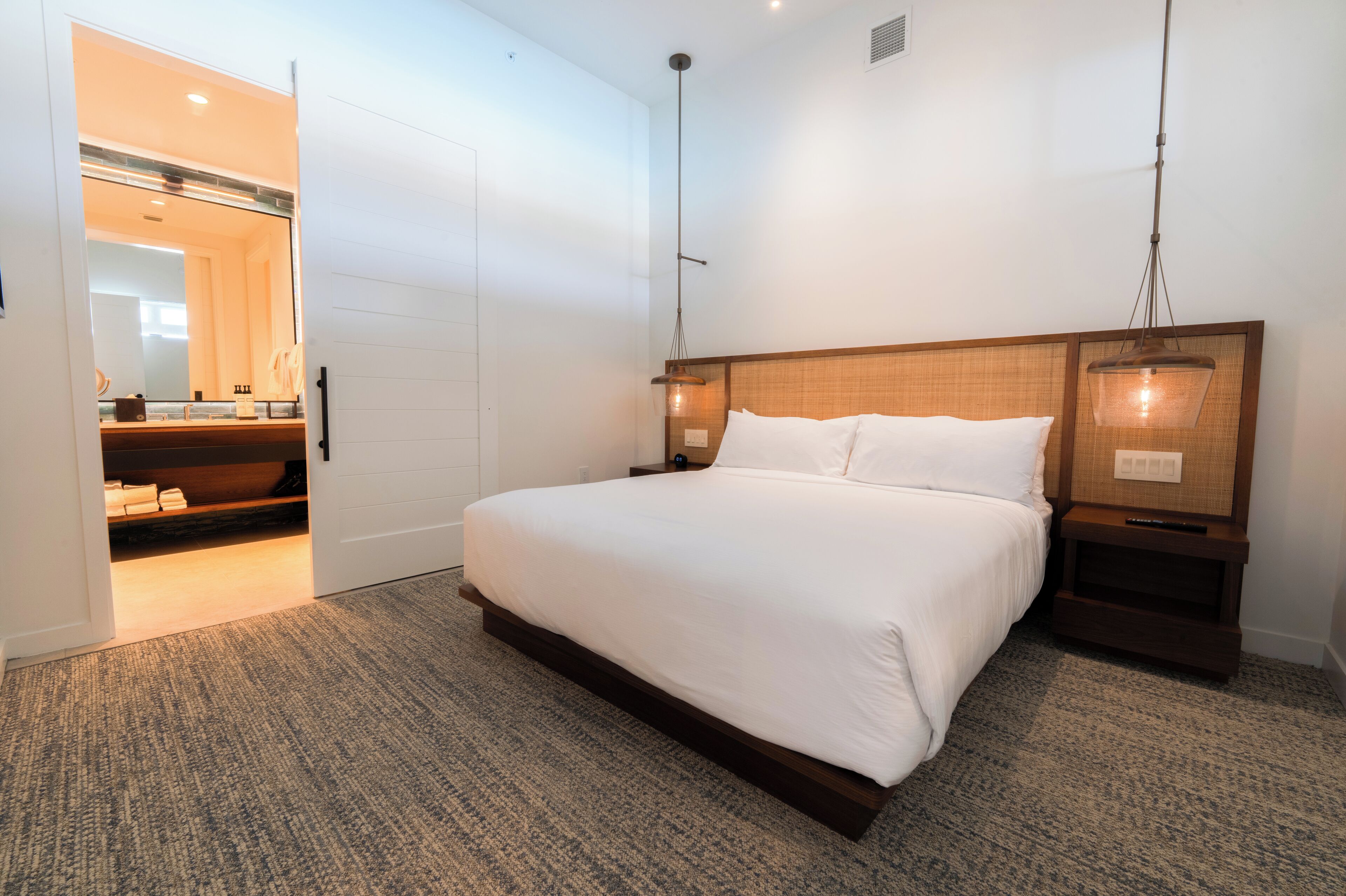 Une chambre d’hôtel moderne avec un grand lit, une tête de lit en bois, des lampes de chevet et un sol recouvert de moquette.