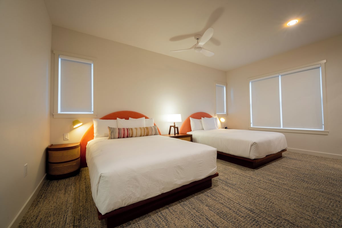 A hotel room with two beds, a ceiling fan, and a carpeted floor.