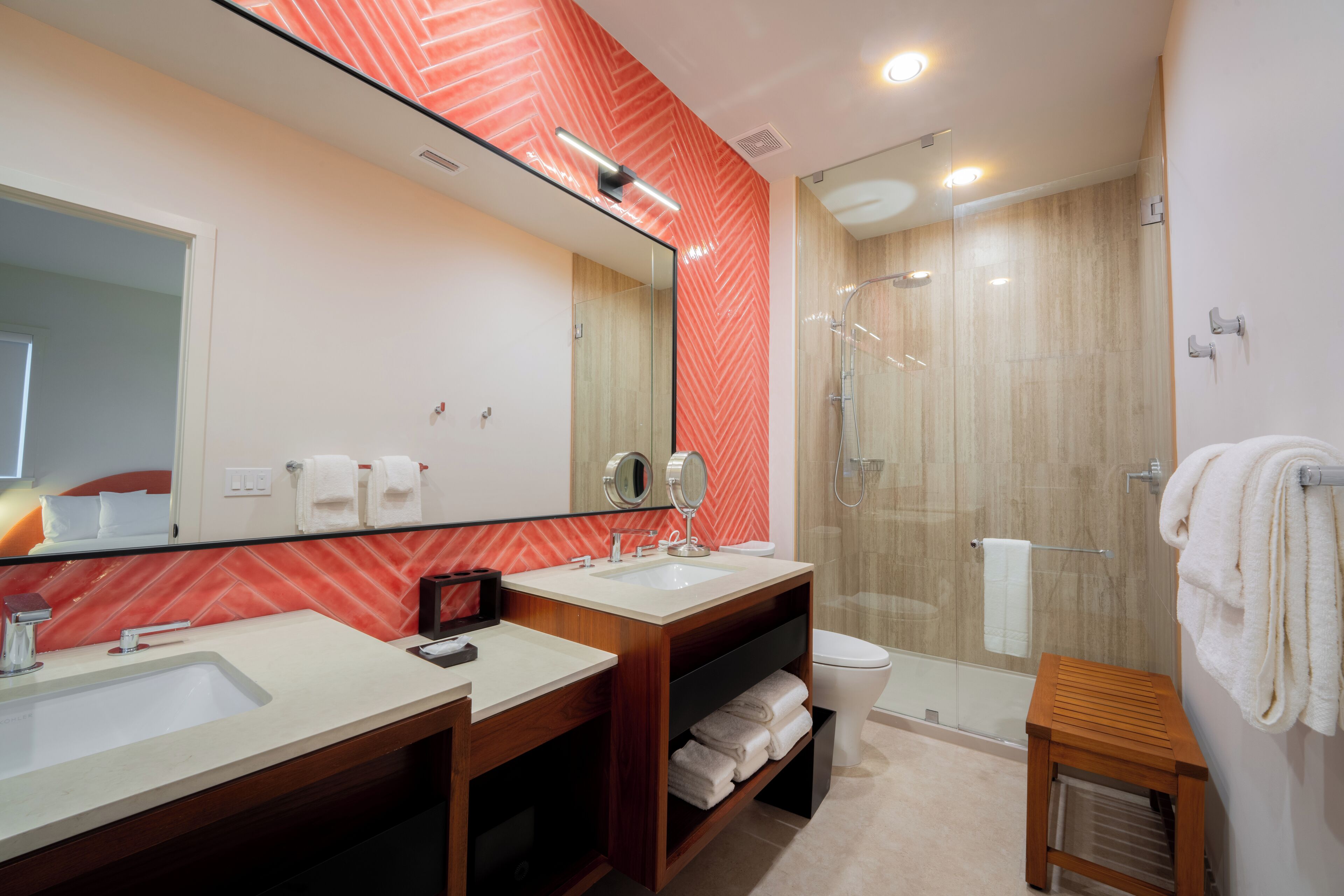A modern bathroom with two sinks, a large mirror, a shower enclosure, and a small wooden stool.