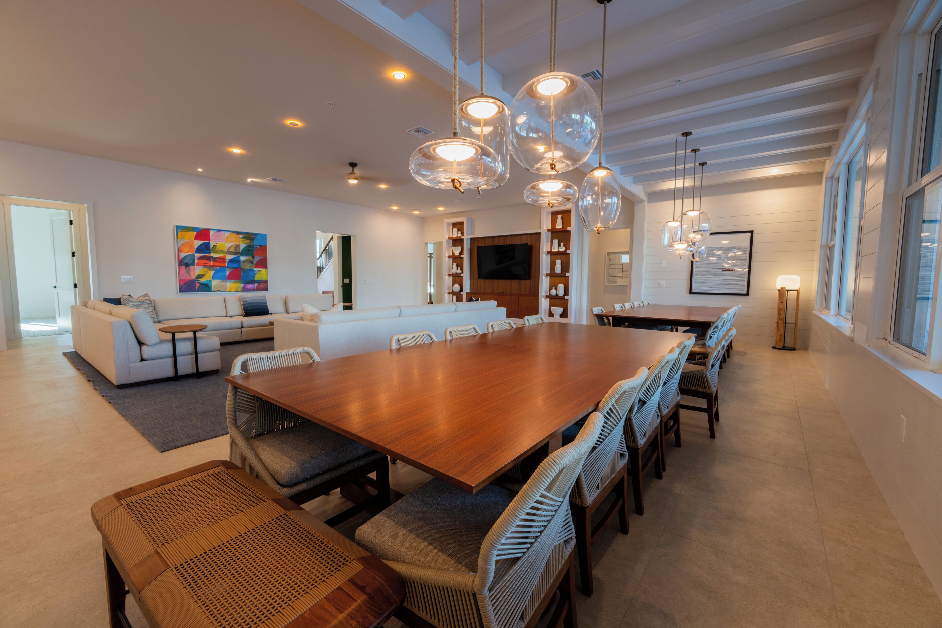 A spacious living room with a large wooden dining table, comfortable seating, and modern lighting fixtures.
