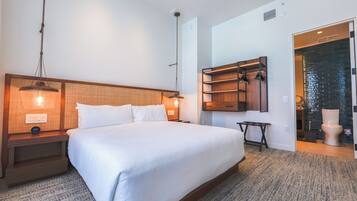 Een moderne hotelkamer met een groot bed, een houten hoofdbord, nachtkastjes met lampen, een inbouwkastje en uitzicht op de badkamer.