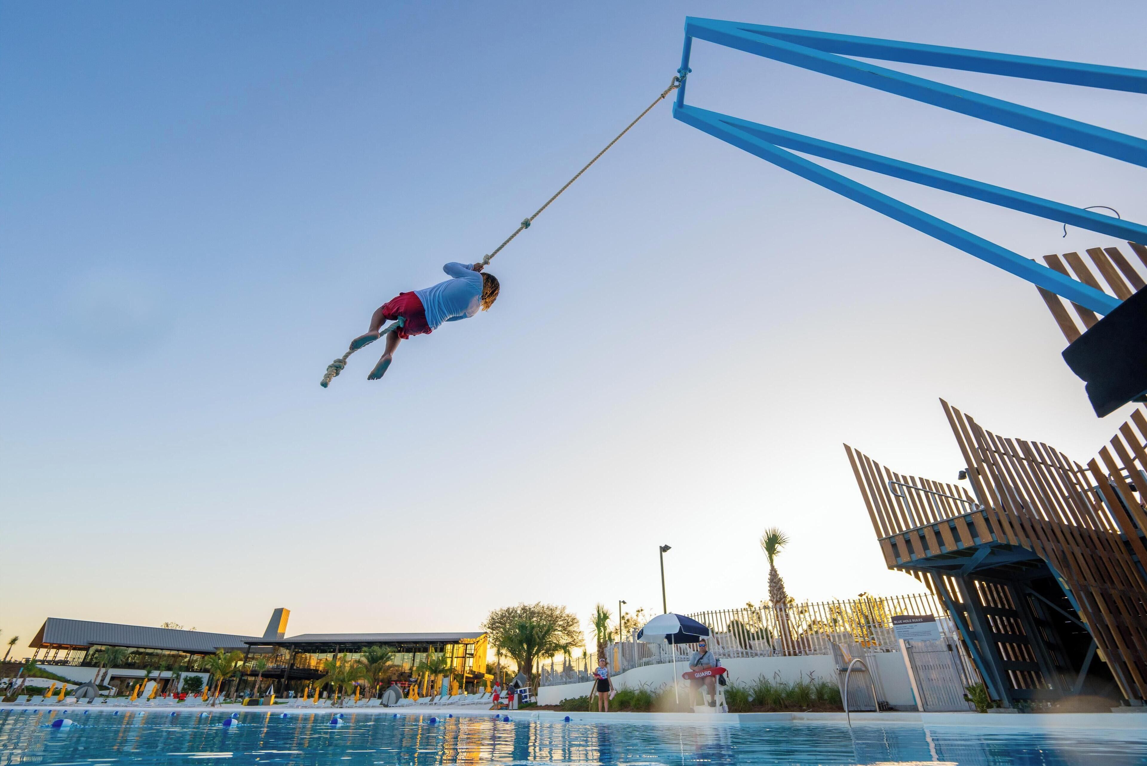 A person performing a high dive stunt at a pool.