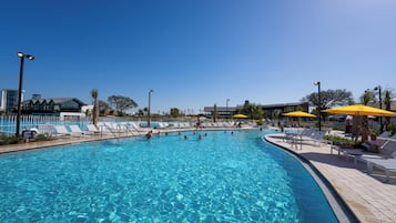 A swimming pool with clear blue water, surrounded by lounge chairs and umbrellas, and a fence enclosing the area.