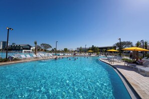 A swimming pool with clear blue water, surrounded by lounge chairs and umbrellas, and a fence enclosing the area. - Evermore Orlando Resort (Orlando)