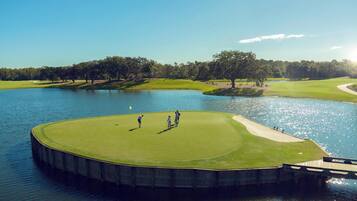 A golf course with a water body, trees, and a clear sky.
