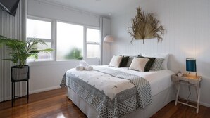 A bedroom with a bed, a bedside table, a lamp, a potted plant, and a window. - Boho Beach Lux 250 Meters to Burleigh Sands (Burleigh Heads)