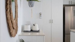 A modern kitchen with white cabinetry, a stainless steel refrigerator, and a hanging plant. - Boho Beach Lux 250 Meters to Burleigh Sands (Burleigh Heads)