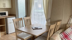 A compact living space with a dining table, chairs, a sofa, a microwave, and a refrigerator. - Beautiful 2-bed Static Caravan (Newton Stewart)