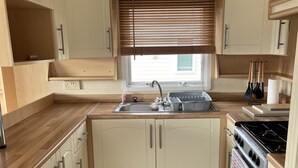 A compact kitchen with wooden countertops, a sink, a stove, and cabinets. - Beautiful 2-bed Static Caravan (Newton Stewart)