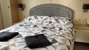 A neatly made bed with a geometric patterned bedspread and two folded towels. - Beautiful 2-bed Static Caravan (Newton Stewart)