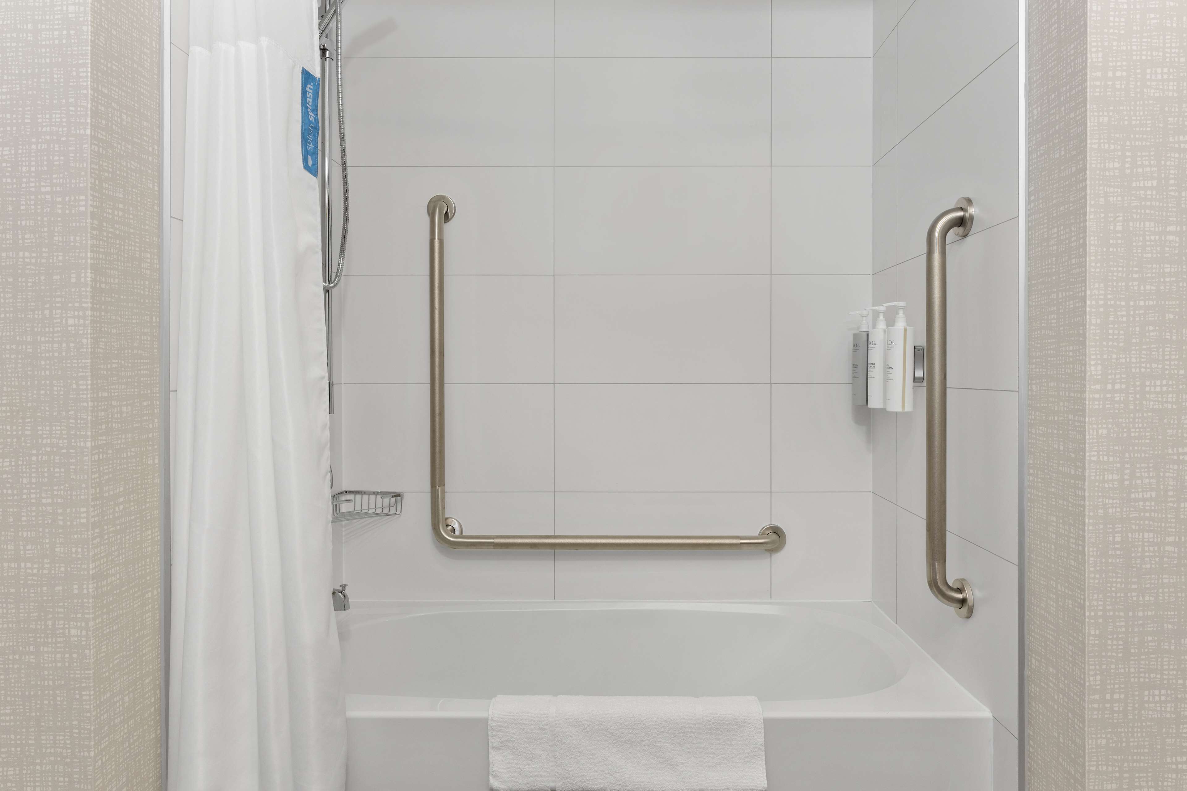 Een moderne badkamer met een bad, handgrepen en een handdoek.