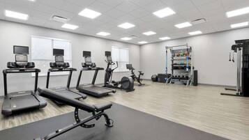 Un gimnasio con cintas de correr, elípticas y equipo de levantamiento de pesas.