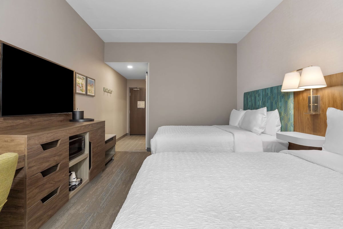 A hotel room with two beds, a TV, a wooden desk, and a lamp.