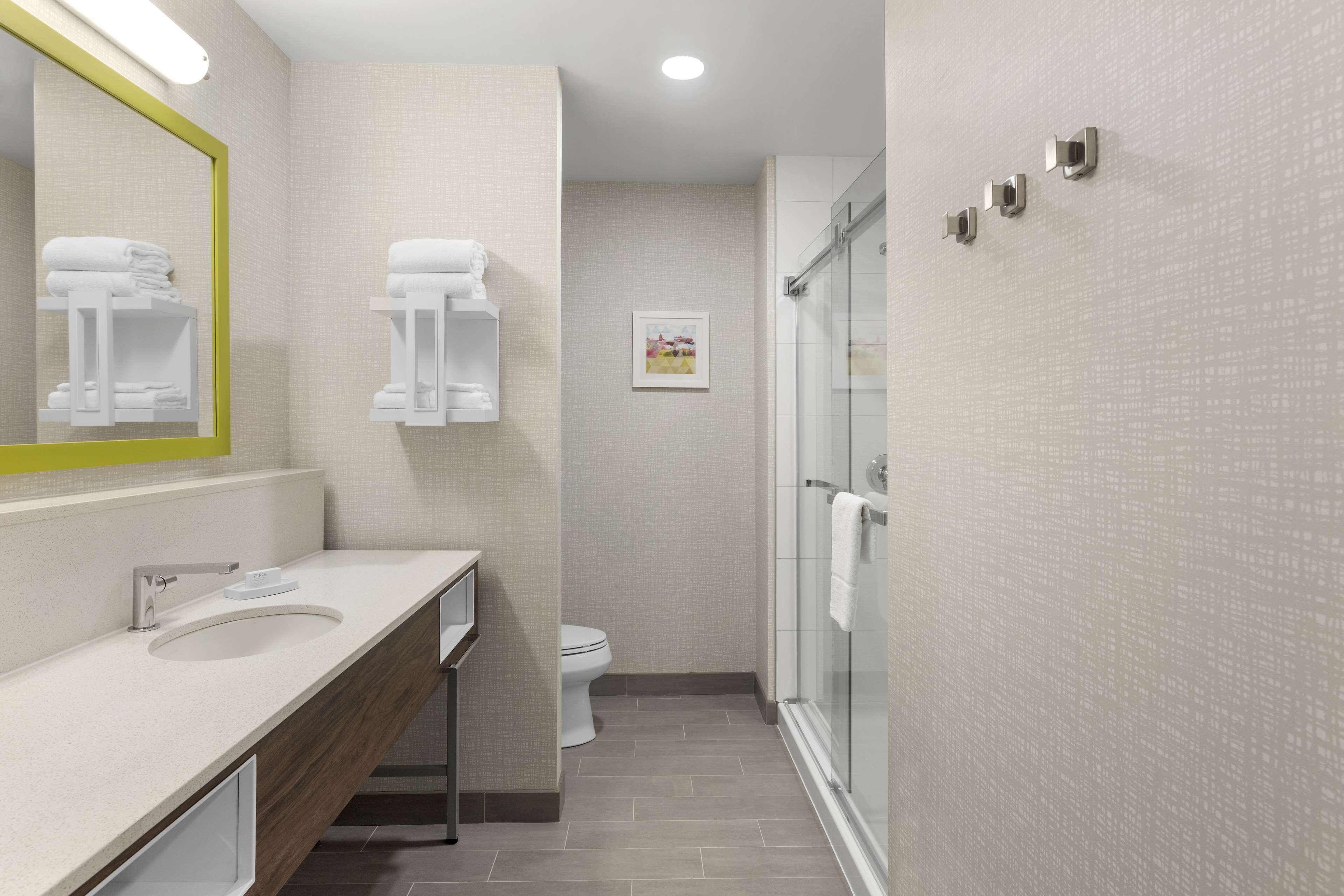 A modern bathroom with a large mirror, a sink, a toilet, and a shower area.