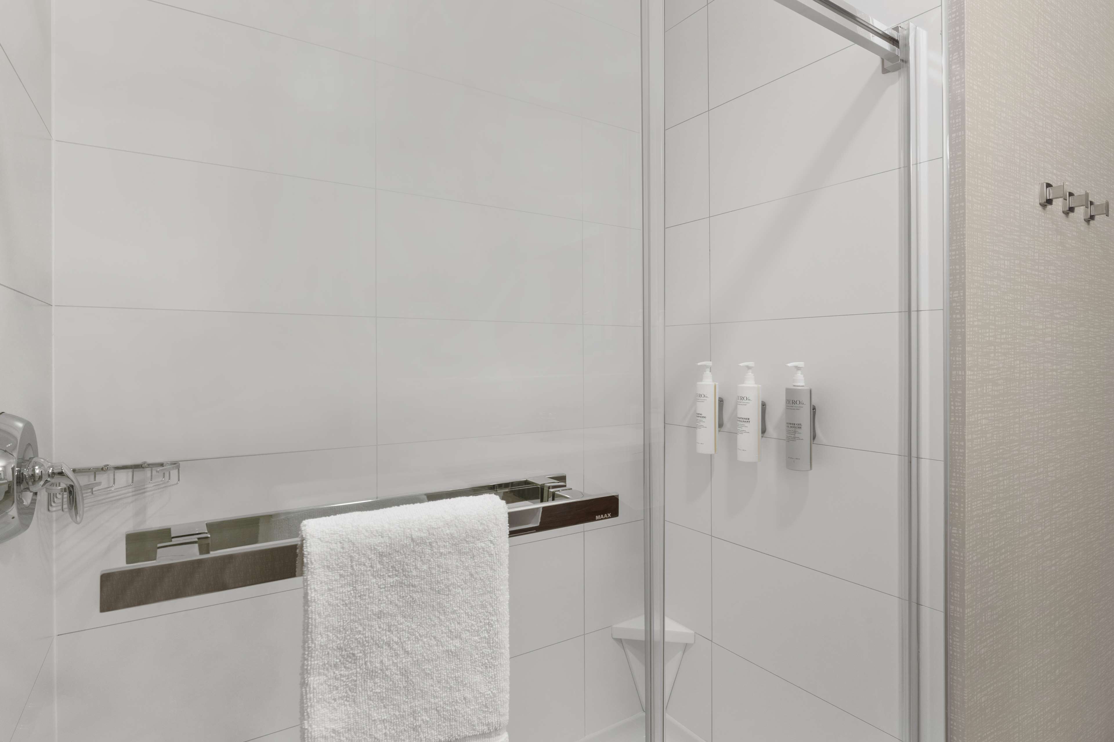 A modern bathroom with a glass shower enclosure, a white towel, and toiletries on a shelf.