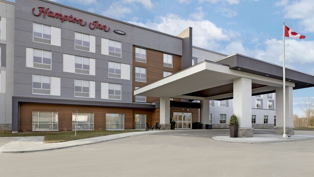 A Hampton Inn hotel with a modern facade, a covered entrance, and a flagpole.