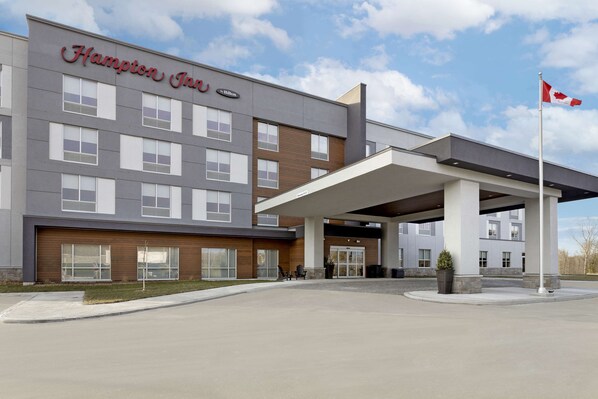 A Hampton Inn hotel with a modern facade, a covered entrance, and a flagpole.