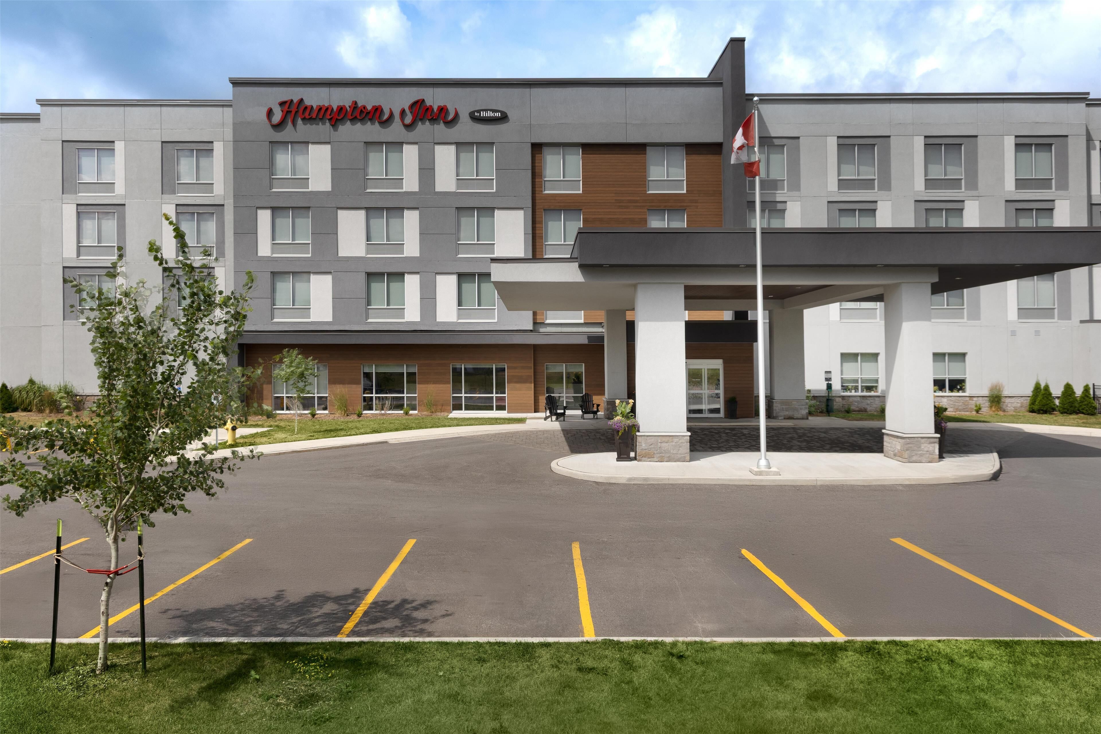 A Hampton Inn hotel with a modern facade, a parking lot, and a flagpole.