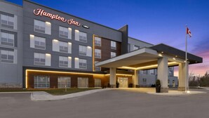 A modern Hampton Inn hotel with a covered entrance and a flag.