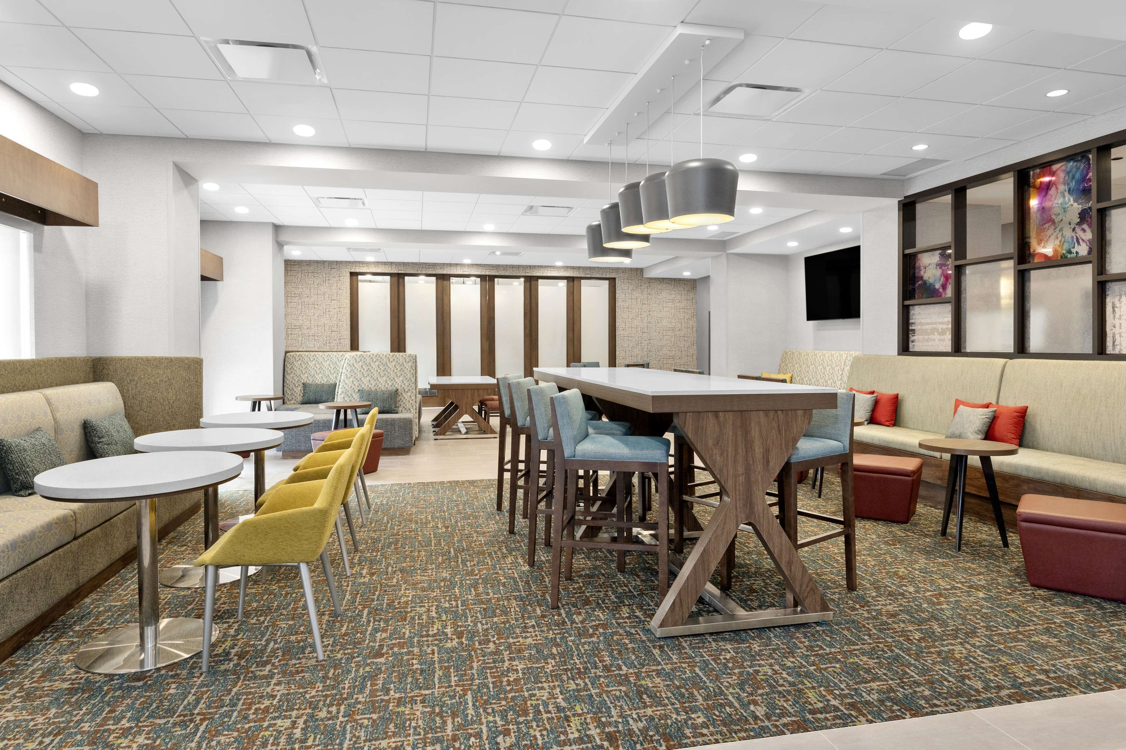 Una moderna hall d'albergo con diverse zone relax, tra cui divani, poltrone e un lungo tavolo condiviso.