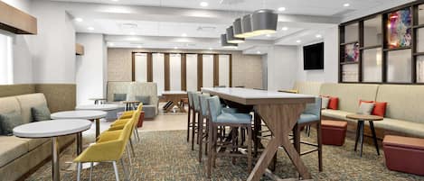 Una moderna hall d'albergo con diverse zone relax, tra cui divani, poltrone e un lungo tavolo condiviso.