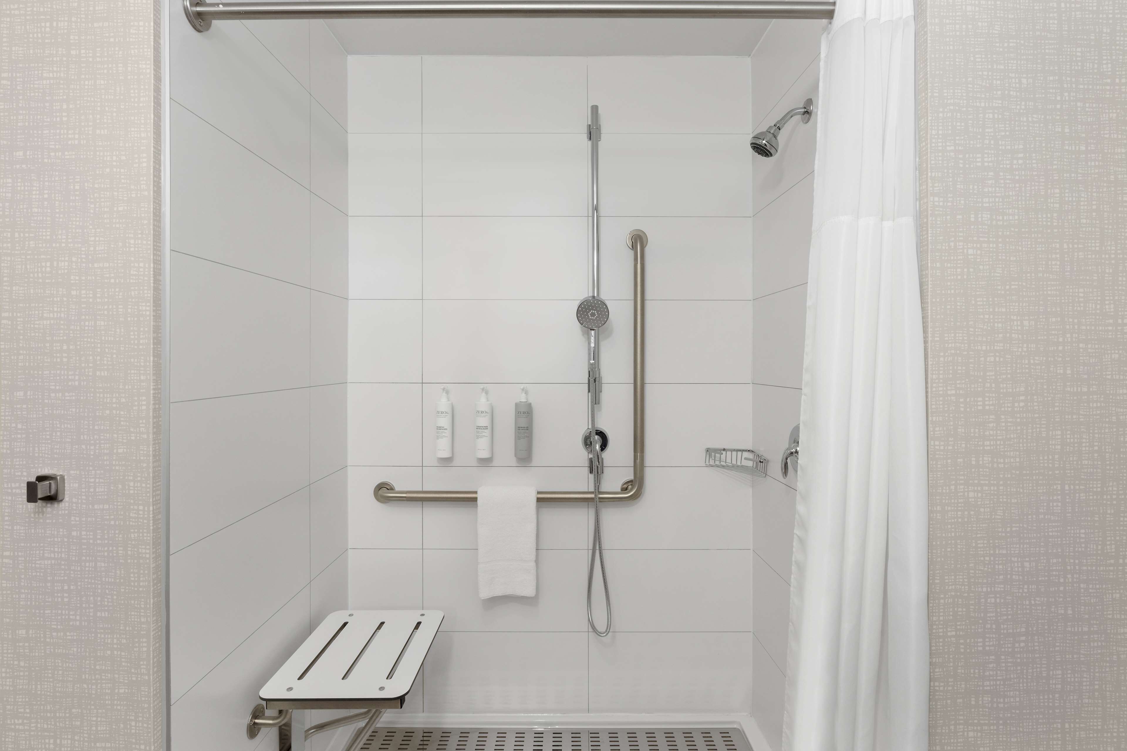 A modern shower area with a grab bar, a handheld showerhead, and a handheld showerhead mounted on the wall.