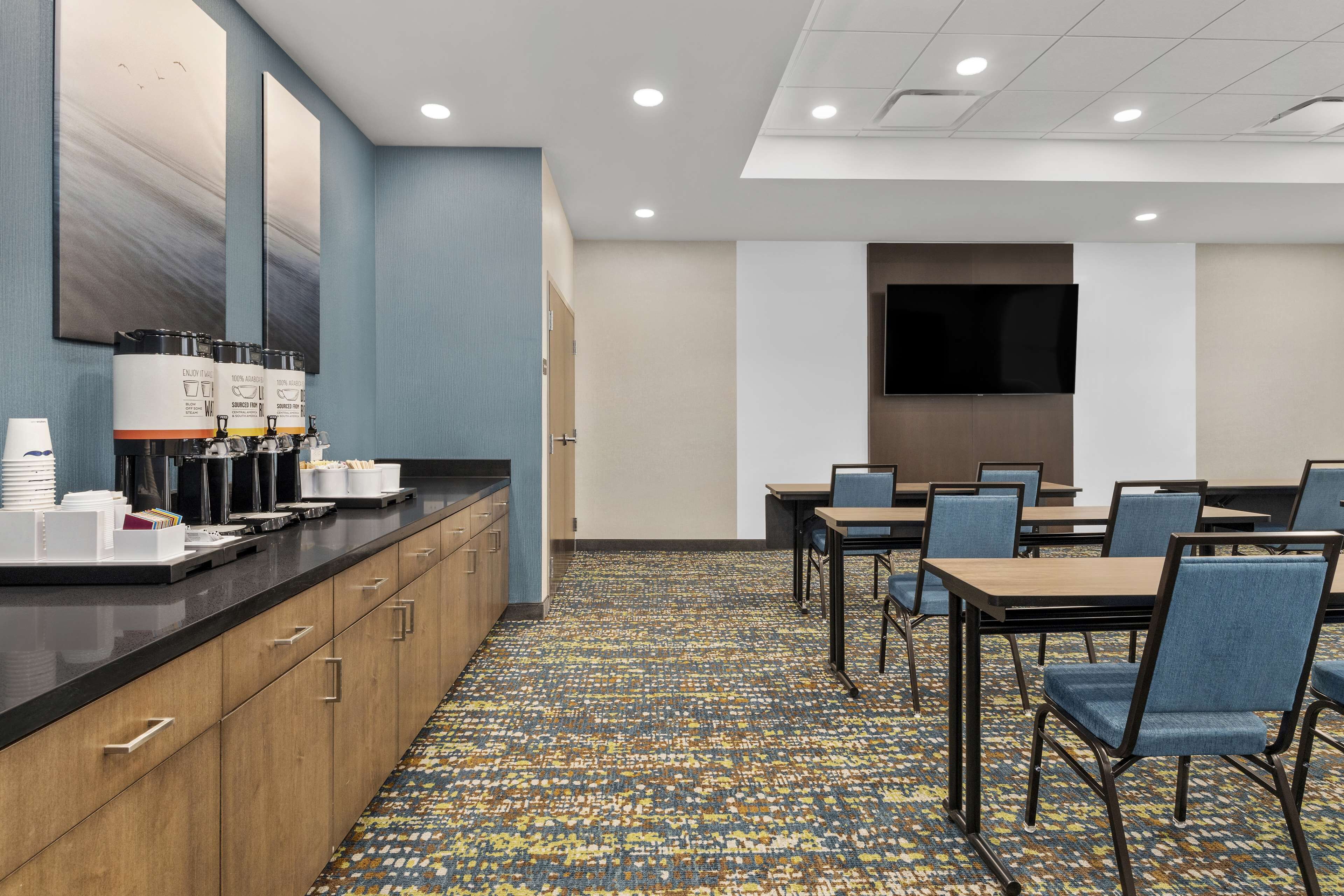 A hotel conference room with a long counter, multiple chairs, and a flat-screen TV on the wall.
