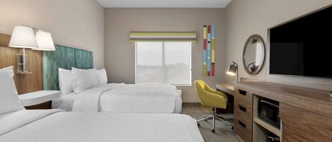Habitación de hotel con dos camas, un escritorio con silla, televisión y ventana con vistas.