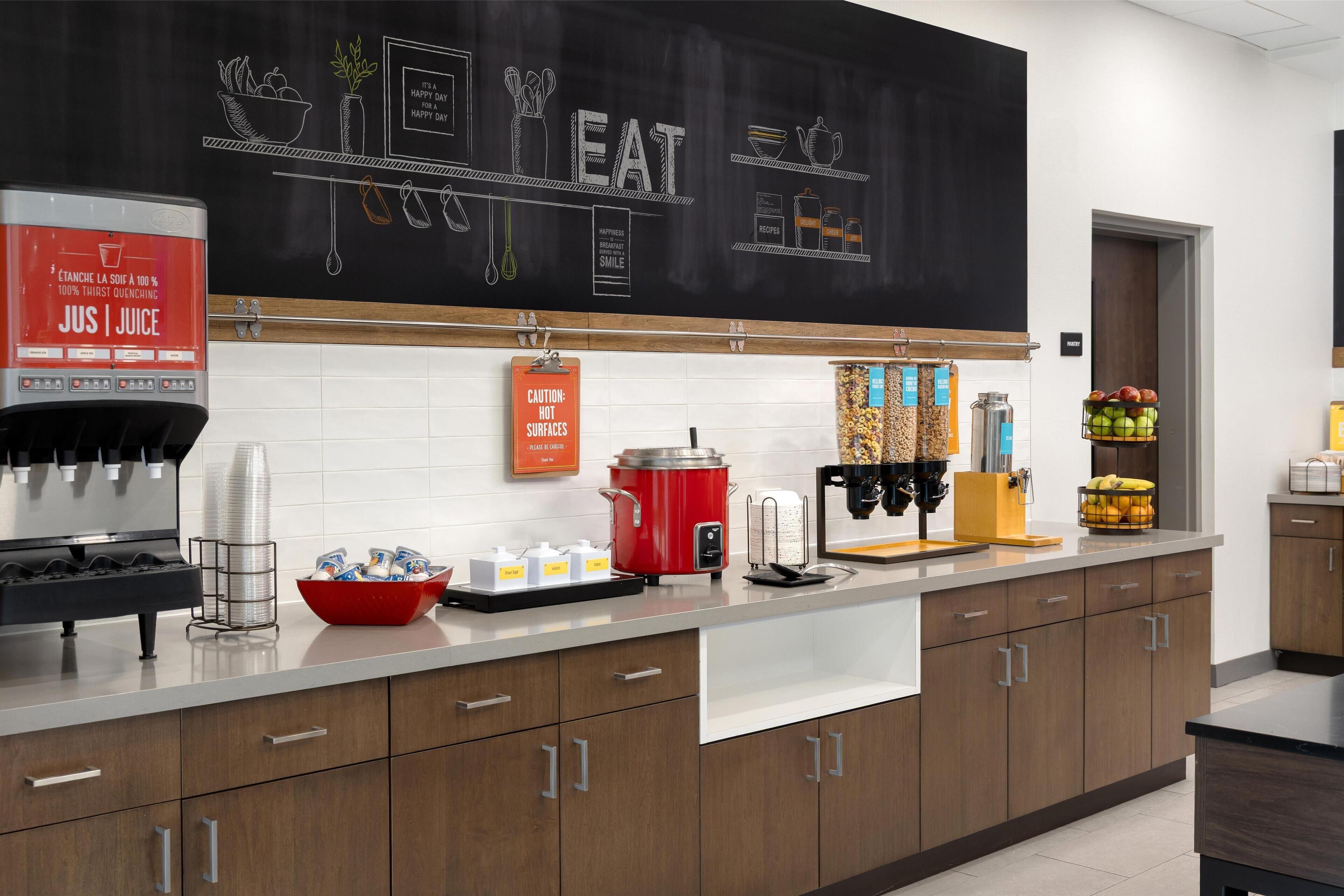 A modern kitchen with a chalkboard displaying 'EAT' and kitchen utensils, a coffee machine, a red slow cooker, and various food items on the counter.