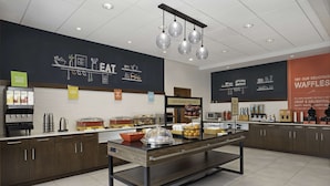 A breakfast buffet area with various food stations, including a sign for 'Happy Breakfast Starts Here' and a display for waffles.