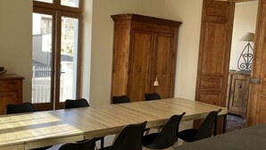 A dining area with a wooden table and black chairs, a wooden cabinet, and a large window with a view of buildings outside.