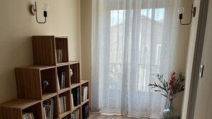 A room with a wooden bookshelf, a window with sheer curtains, and a vase with flowers.