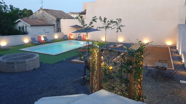 A backyard with a swimming pool, lounge chairs, a barbecue grill, and a table with chairs.