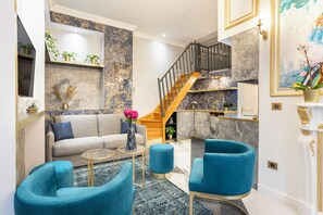 A modern living room with a sofa, two blue armchairs, a coffee table, and a staircase leading to a kitchen area. - Merveil - Luxury Suite - Notre-Dame - Saint Louis (Paris)