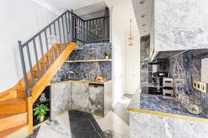 A modern kitchen with a marble backsplash, a wooden staircase, and a built-in oven. - Merveil - Luxury Suite - Notre-Dame - Saint Louis (Paris)