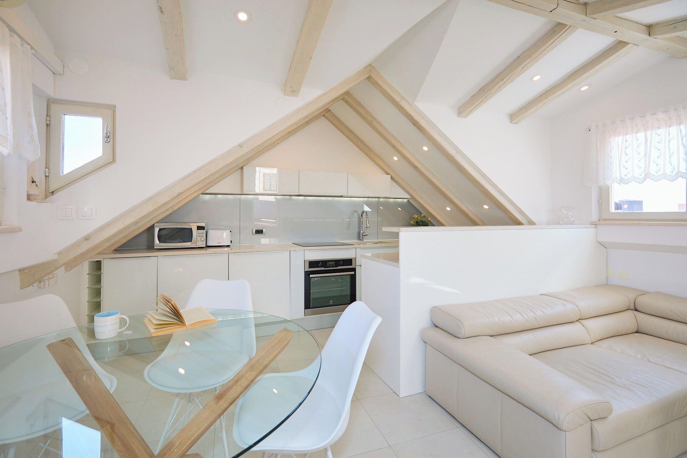 A compact kitchen with modern appliances, a glass dining table, and a beige sofa.