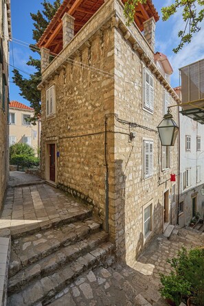 Un bâtiment en pierre doté d’un balcon en bois, d’une porte rouge et d’un petit jardin.
