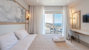 A hotel room with a bed, a desk, a chair, a TV, and a balcony with a view of the sea.