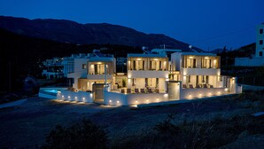 A modern multi-story house with a flat roof, large windows, and a well-lit exterior.