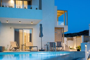 A modern poolside area with lounge chairs, a table, and a covered umbrella.