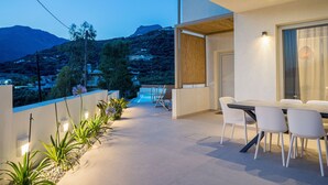 An outdoor patio with a dining table and chairs, surrounded by plants and overlooking a mountainous landscape.