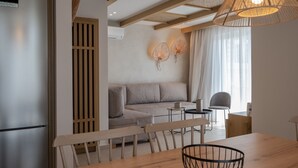 A modern living room with a sofa, dining table, chairs, and a kitchen area with a refrigerator.