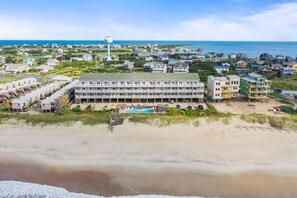 A beachfront hotel with multiple buildings, a swimming pool, and a lighthouse in the background.