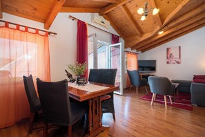 Um quarto aconchegante com teto de madeira, uma mesa de jantar com cadeiras, uma TV e uma janela com cortinas.
