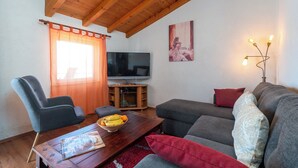 Un salon avec un plafond en bois, une télévision, un canapé, un fauteuil et une table basse sur laquelle se trouve un saladier rempli de fruits.