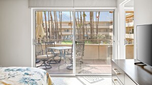 Una habitación de hotel con balcón, una cama, televisor y zona de comedor con sillas y una mesa.