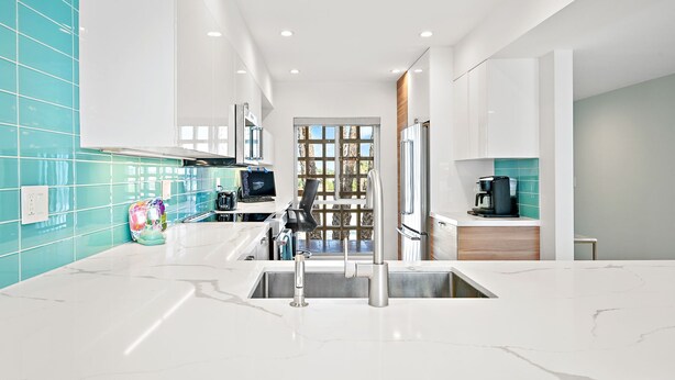 Una cocina moderna con encimeras de mármol blanco, electrodomésticos de acero inoxidable y azulejos de resalte color aguamarina.