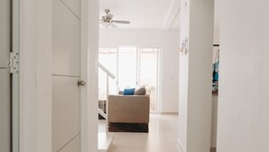 Un couloir mène à un espace de vie comprenant un canapé et un ventilateur de plafond.