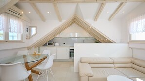 A modern loft-style living space with a glass dining table, white chairs, a beige sofa, and a kitchen in the background. - Hedera Estate, Hedera A22 (Dubrovnik)